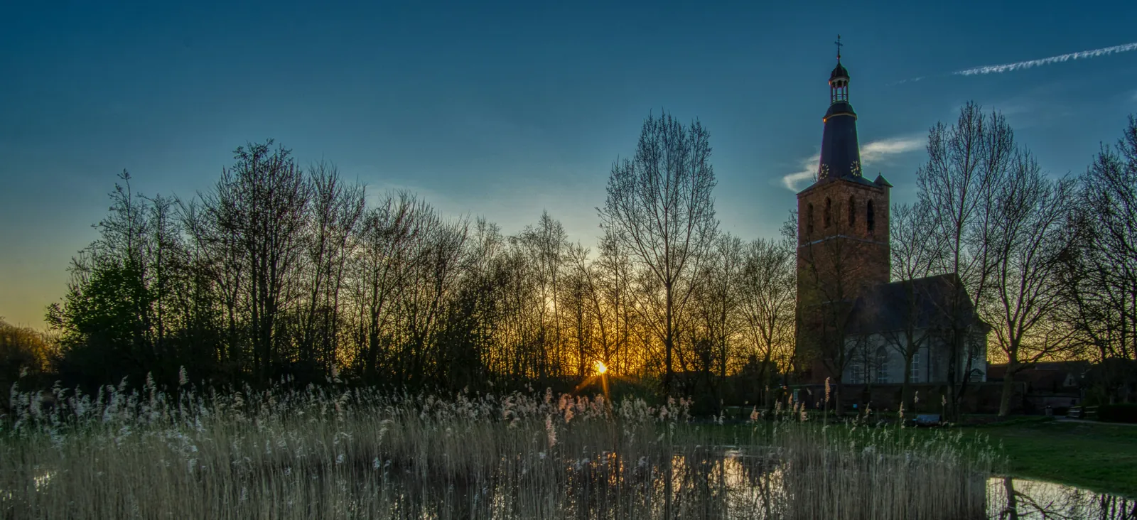 Een kerk naast water en riet bij zonsondergang